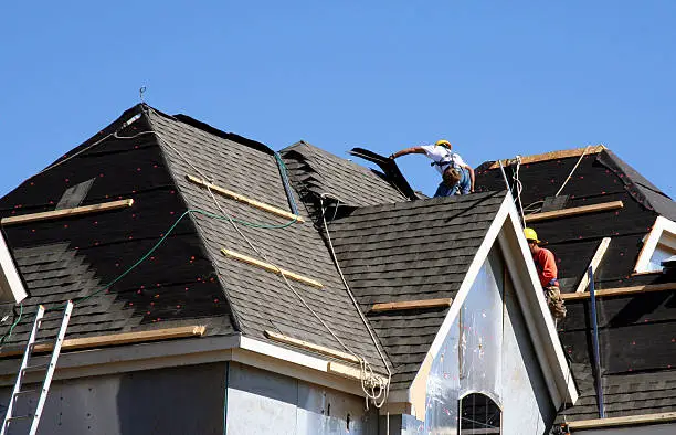 Experienced roofer inspecting shingle alignment and flashing with close attention